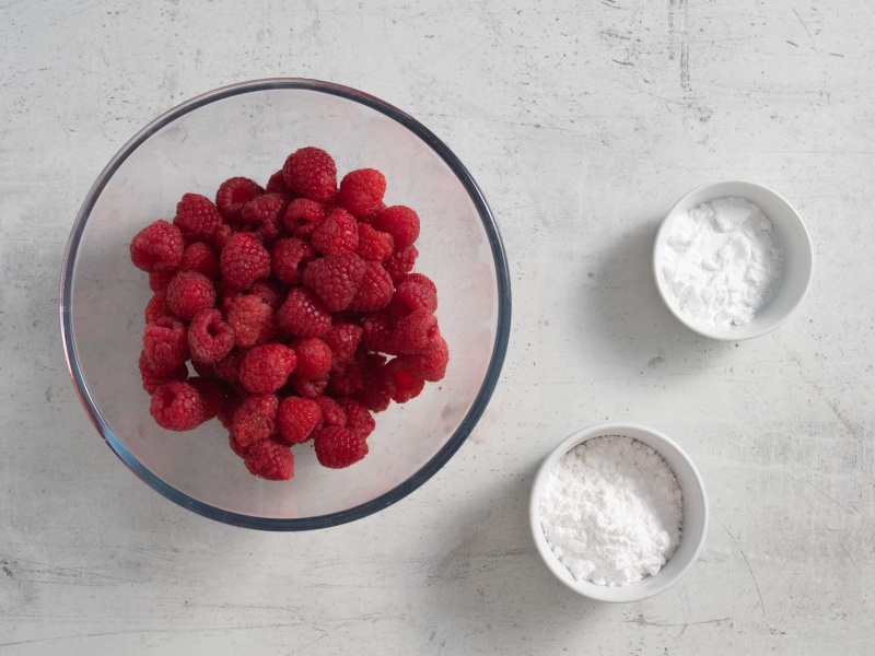W misie maliny. Obok w miseczce cukier puder oraz mąka ziemniaczana.