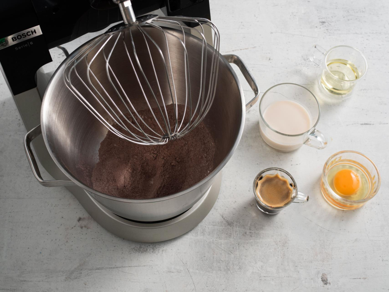 Robot kuchenny na blacie, a obok mokre składniki w miseczkach: espresso, jajko, olej oraz mleko.