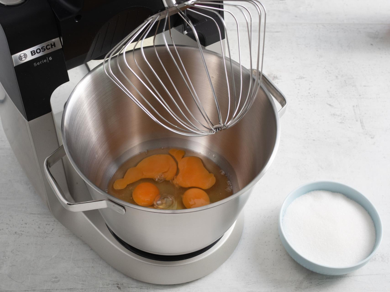 Jajka w misie robota kuchennego. Obok cukier w miseczce.