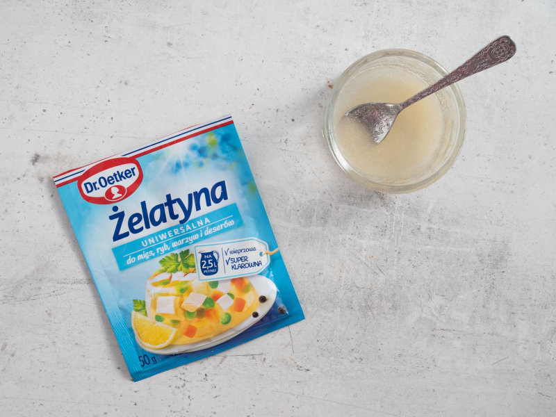 Żelatyna w opakowaniu na blacie. Obok żelatyna zalana zimną wodą.