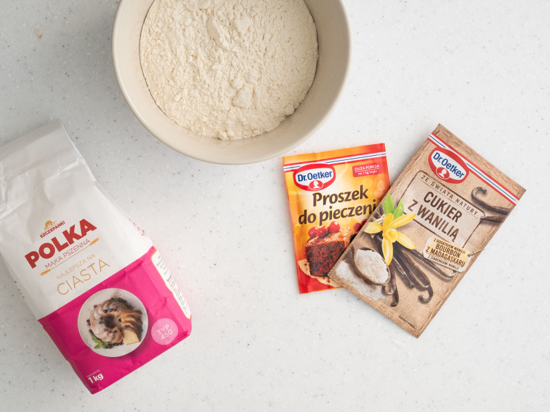 Na blacie kuchennym mąka pszenna, cukier z wanilią oraz proszek do pieczenia.