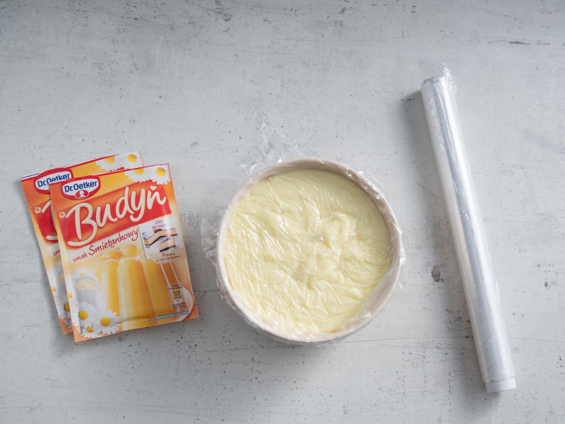 w miseczce budyń przykryty folią obok opakowania budyniu dr. Oetker i folia spożywcza