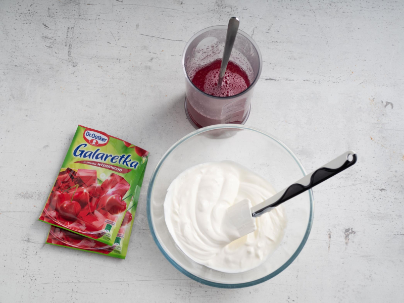 w naczyniu rozpuszczone galaretki wiśniowe Dr. Oetkera obok w szklanej misce jogurt naturalny