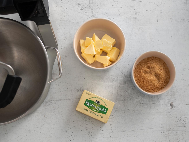 Na blacie kuchennym kostka masła oraz cukier trzcinowy w miseczce.
