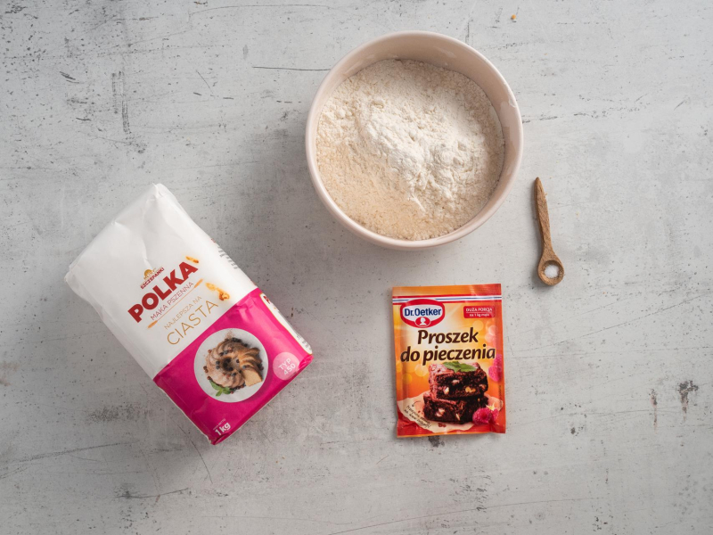 Na blacie kuchennym opakowanie mąki pszennej oraz proszku do pieczenia. W misie mąka pszenna i szczypta soli na drewnianej łyżeczce.
