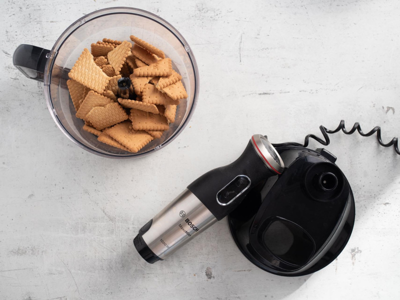 Na blacie kuchennym blender ręczny. Obok herbatniki w pojemniku.