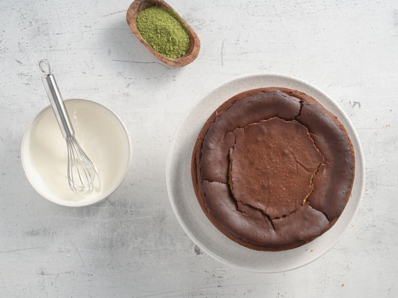 Na blacie upieczony sernik, polewa ze śmietany i herbata matcha.