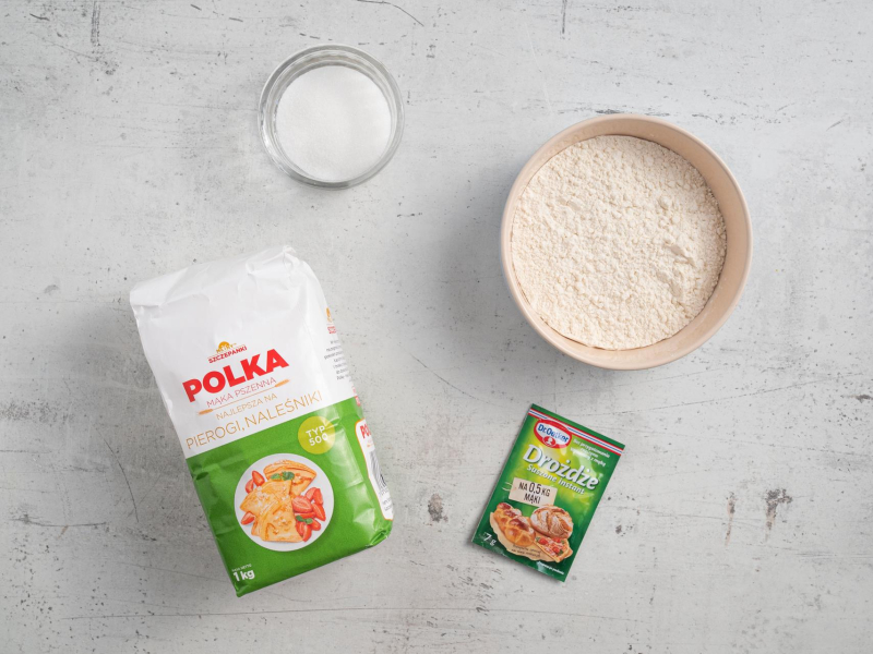 Na blacie kuchennym opakowanie mąki, drożdże oraz mąka  w misce oraz cukier.