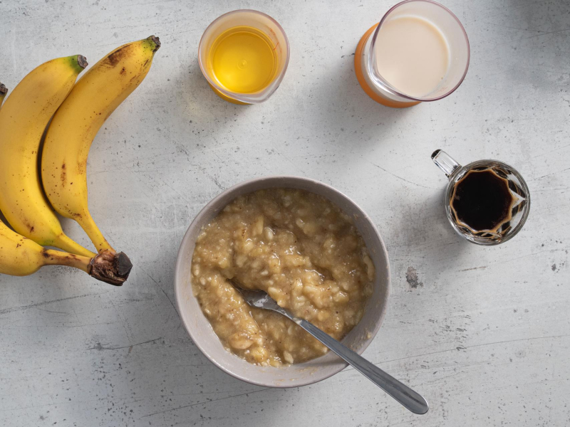 Rozgniecione banany w miseczce. Obok mleko, olej oraz espresso.