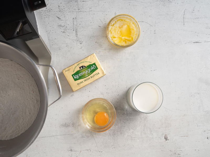 Na blacie kuchennym opakowanie masła, jajko, mleko oraz masło w miseczkach.