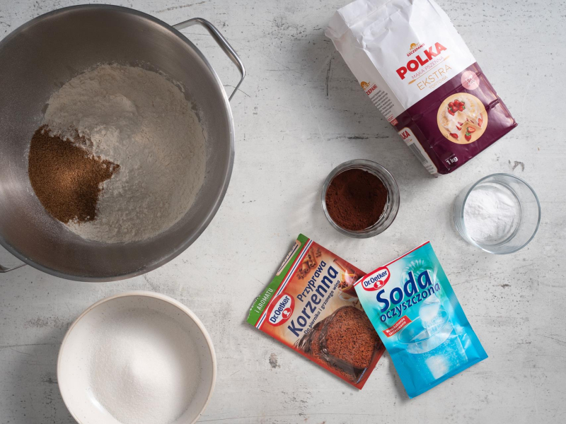 Na blacie kuchennym miska z suchymi składnikami oraz inne suche składniki potrzebne do przygotowania ciasta na pierniczki.
