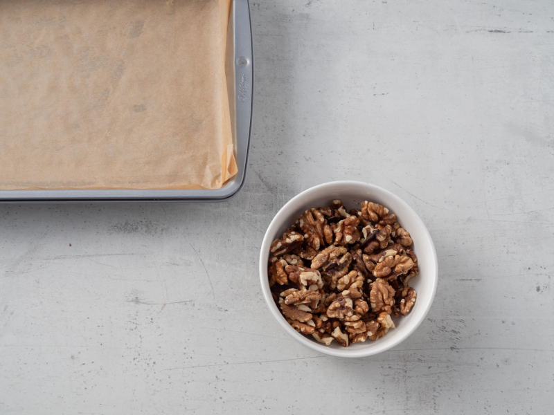 w miseczce uprażone orzechy włoskie obok wyłożona papierem forma do pieczenia
