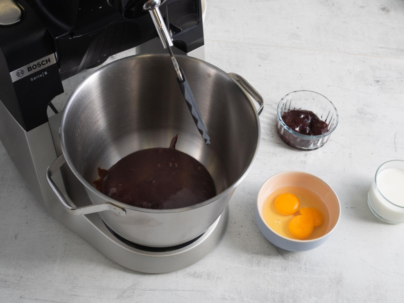 W garnku masa miodowo-korzenna, obok mikser ręczny firmy Bosch, jajka, powidła śliwkowe i mleko.