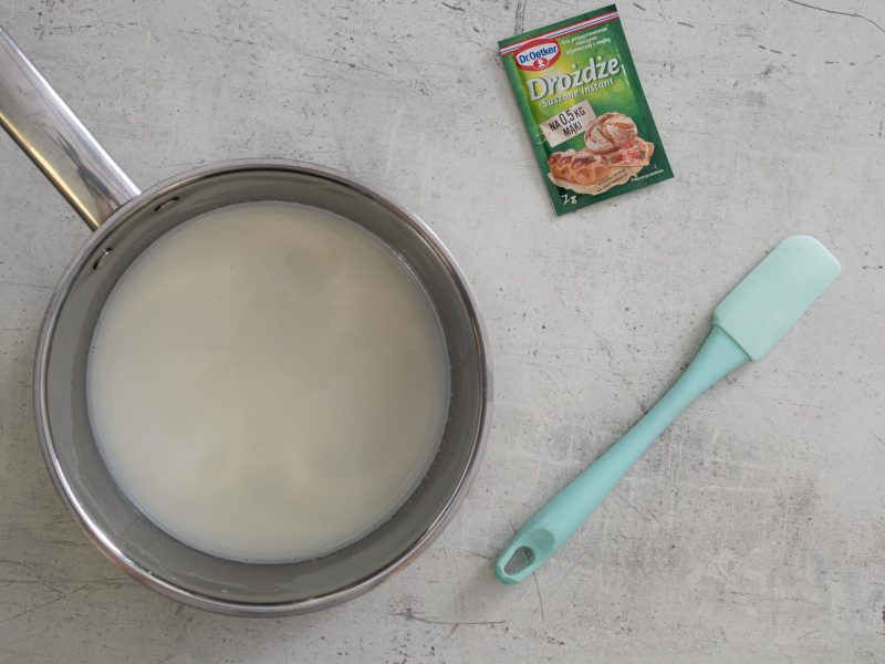 W garnku podgrzane mleko z cukrem. Obok na blacie opakowanie suszonych drożdży.