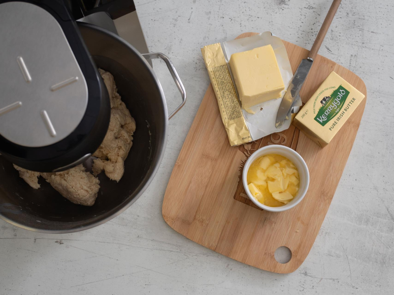 Zagniatanie ciasta drożdżowego w misie. Obok na drewnianej desce masło.