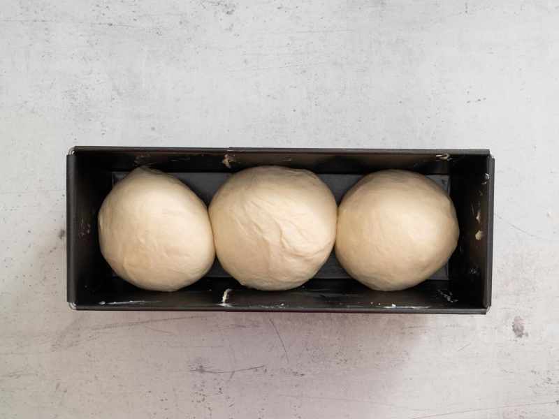 Kulki ciasta drożdżowego ułożone w keksówce.