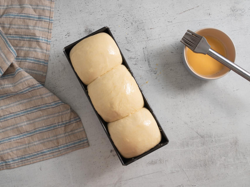 Wyrośnięty chlebek tostowy posmarowany jajkiem.