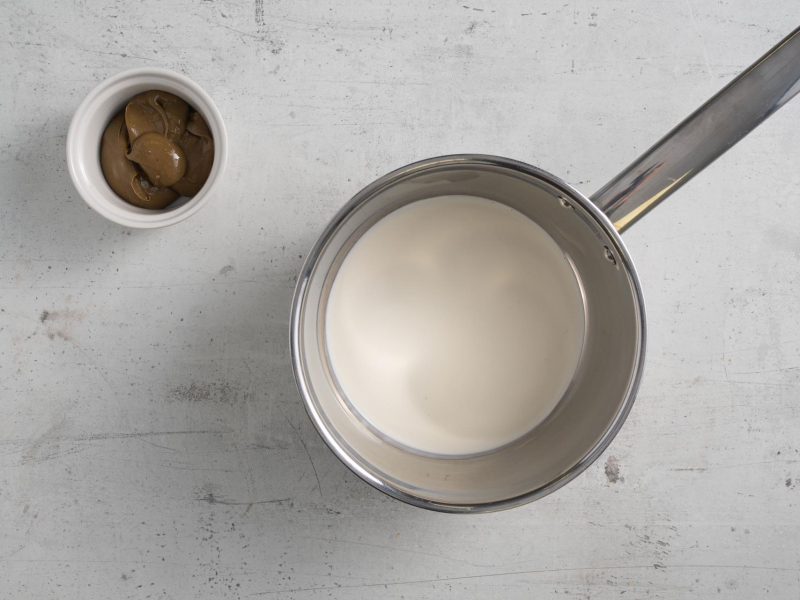 W garnku śmietanka. Obok w miseczce pasta pistacjowa.