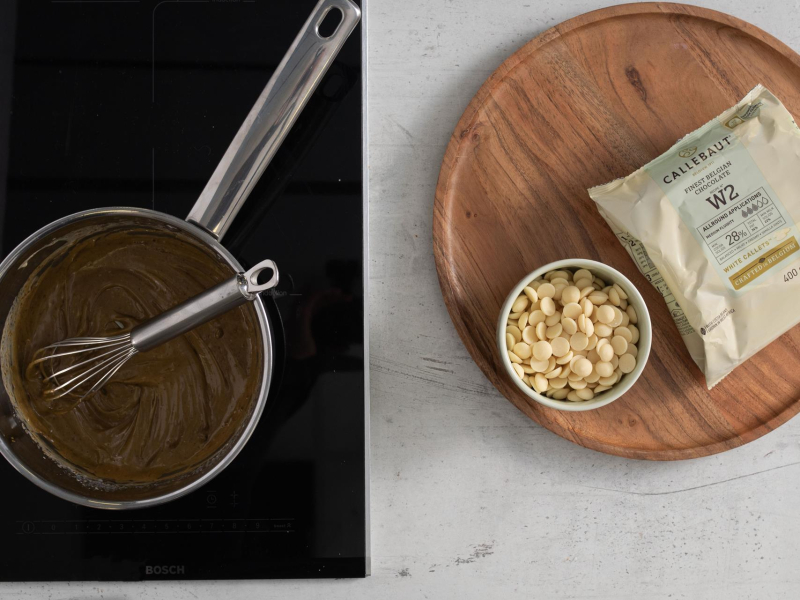 W garnku masa pistacjowa. Obok biała czekolada w kaletkach.