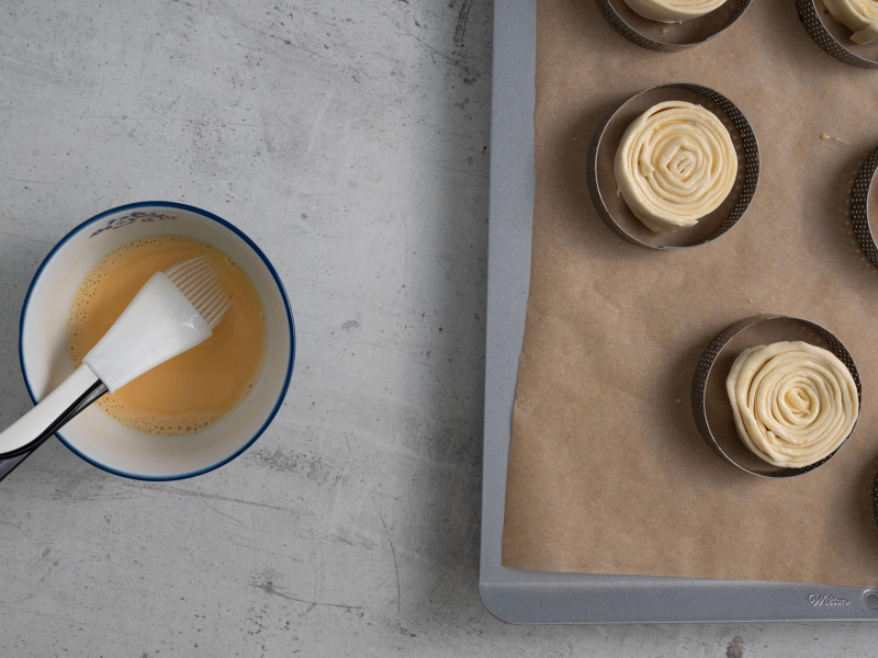 Jajko z mlekiem w miseczce. Obok rollsy na papierze do pieczenia i w rancie.