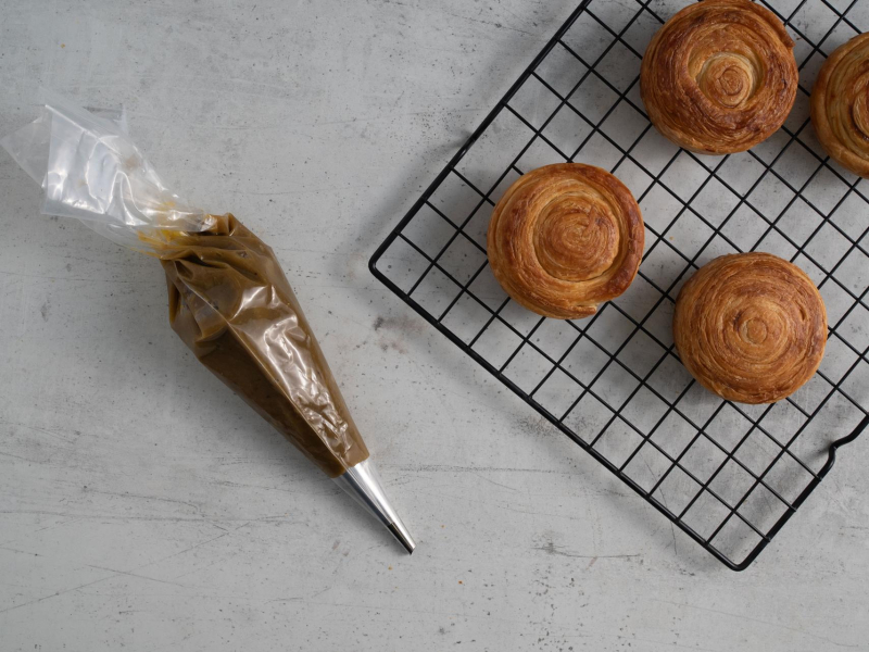 Upieczone rollsy z ciasta francuskiego oraz ganache pistacjowy w rękawie cukierniczym.