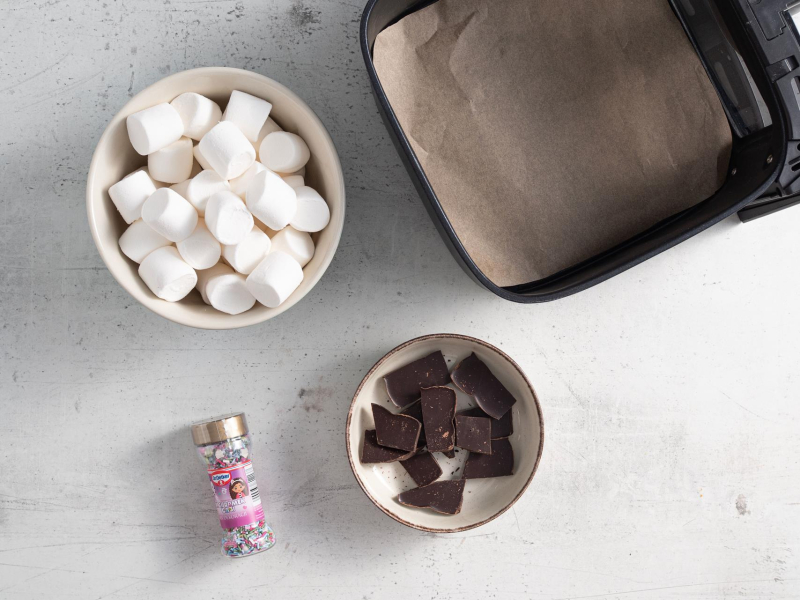 Pianki marshmallow w miseczce. Obok czekolada w miseczce oraz dekoracje cukrowe.