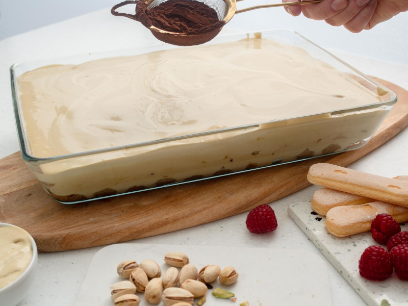 duża foremka z pistacjowym tiramisu posypywana kakao