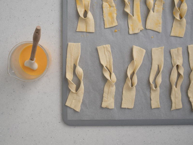 na blaszce ułożone faworki posmarowane jajkiem