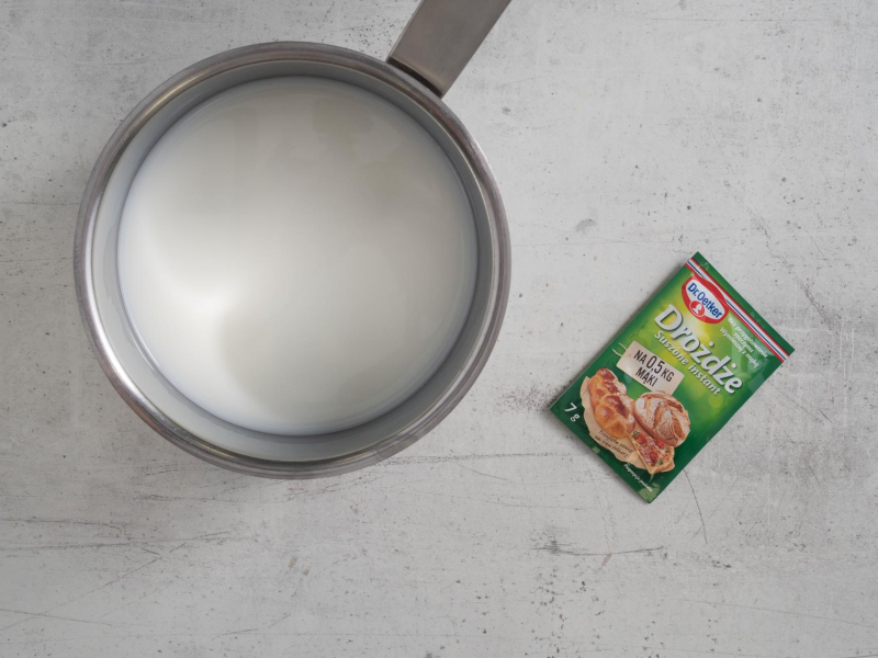 Mleko wymieszane z wodą w garnku. Obok opakowanie drożdży suszonych.