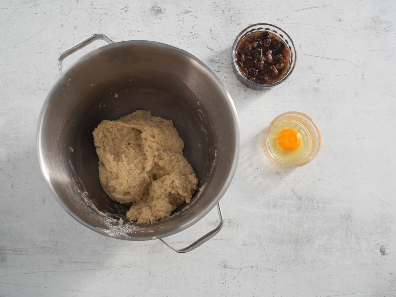 W misie ciasto drożdżowe, a obok jajko w miseczce oraz rodzynki.