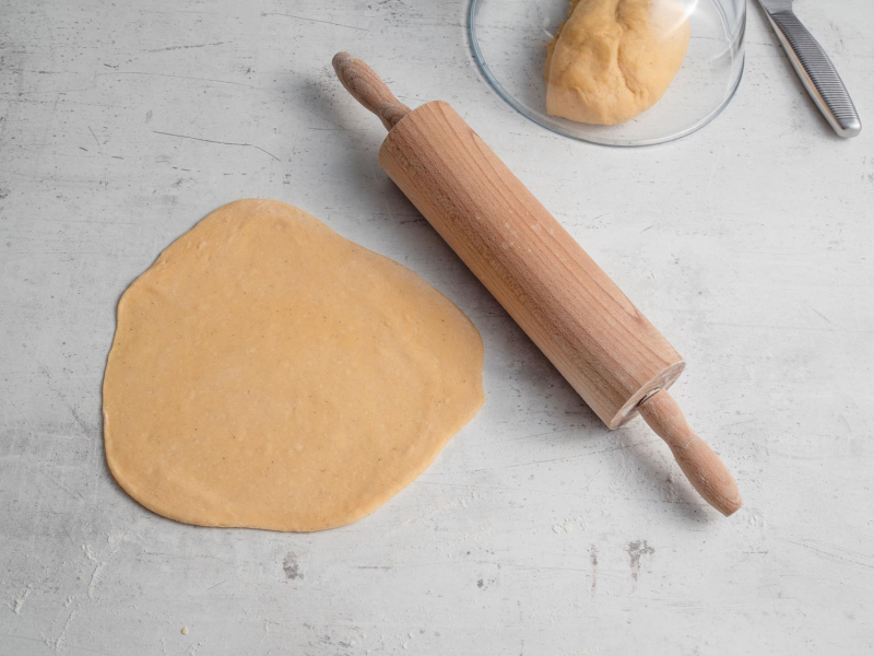 rozwałkowany placek ciasta na faworki obok wałek na blacie