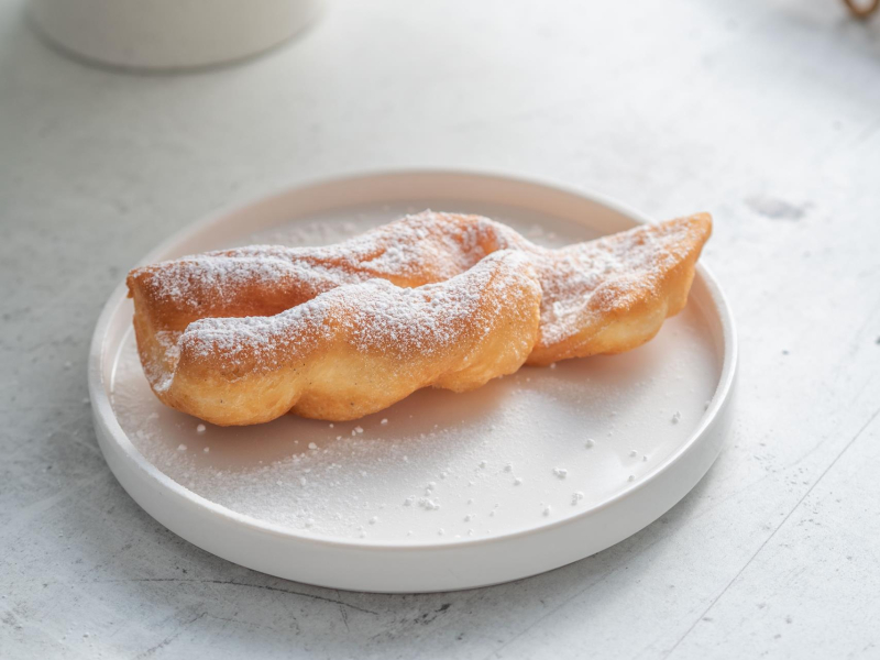 na talerzyku świeżo usmażony faworek posypany cukrem pudrem