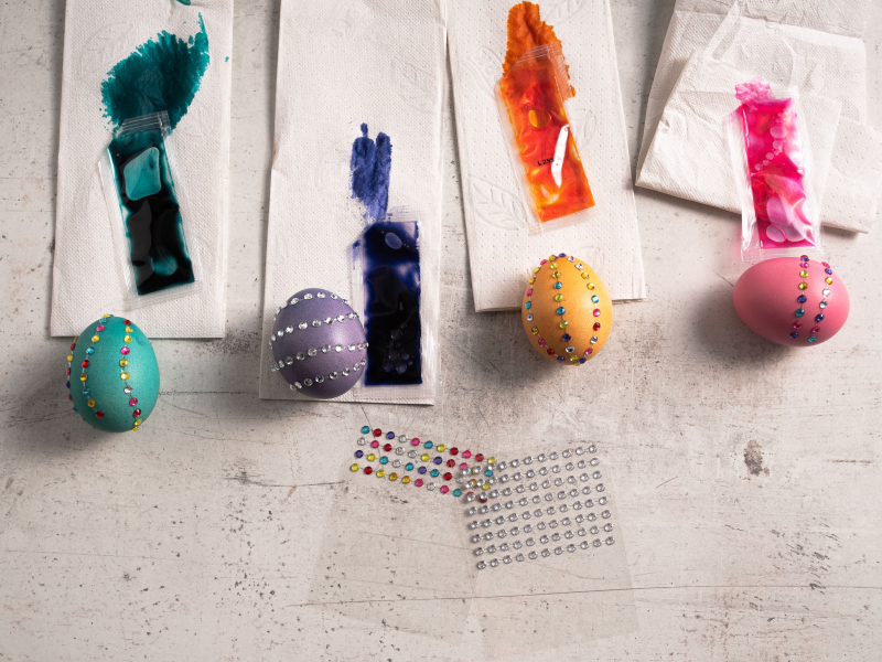 zabarwione jajka na papierowych ręcznikach, obok arkusze z naklejkami w kształcie kryształków