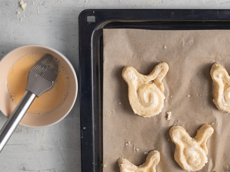 Na blasze do pieczenia drożdżowe króliczki z serem przed upieczeniem.