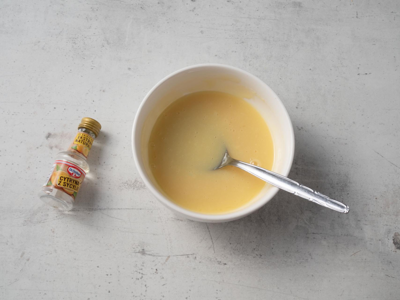 w miseczce przygotowana polewa z białej czekolady do sernika obok ekstrakt cytrynowy