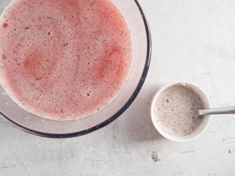 Na blacie kuchennym miska ze zmiksowanymi truskawkami i miętą. Obok żelatyna w miseczce rozmieszczana z częścią zblendowanych truskawek.