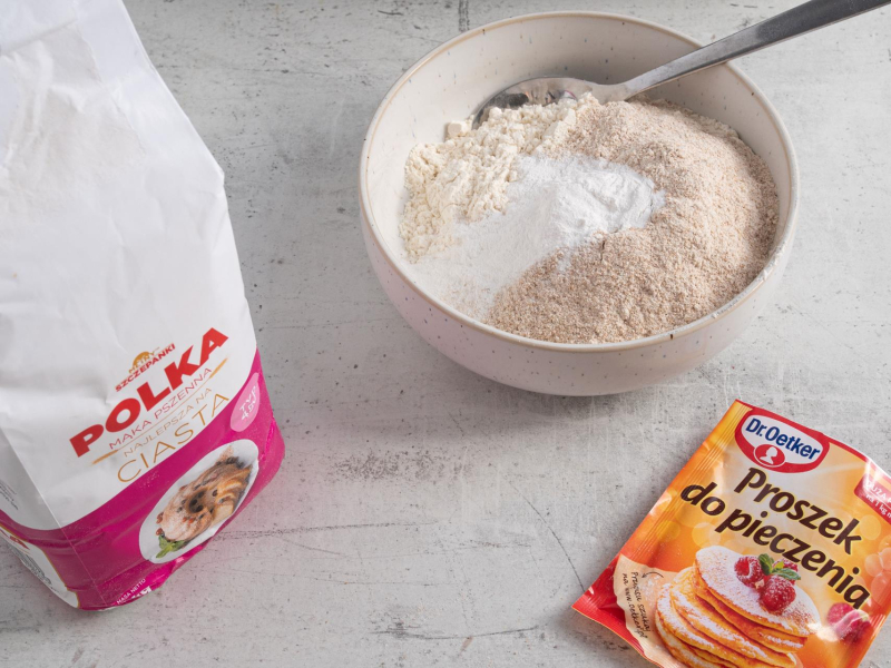 Opakowanie mąki stojące na blacie. Obok opakowanie proszku do pieczenia i wymieszane suche składniki w miseczce.