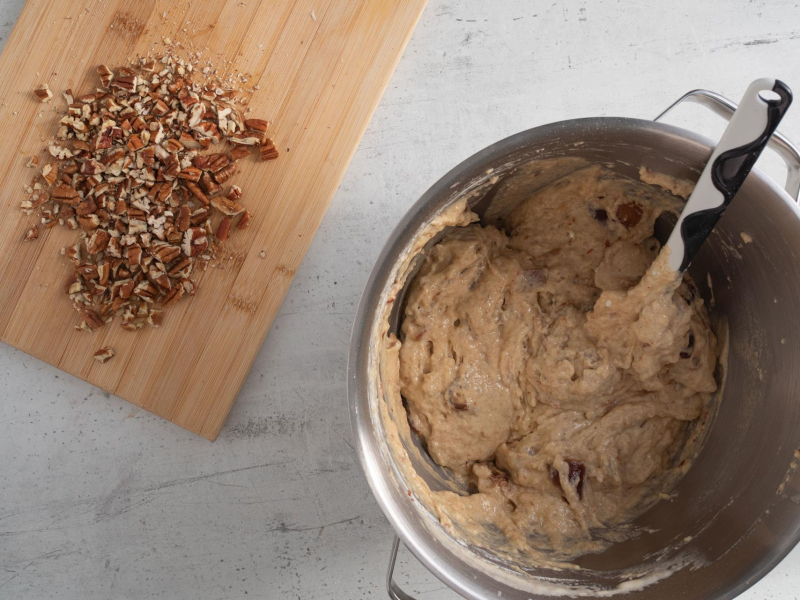 W misie wymieszane ciasto na chlebek daktylowy. Obok na desce kuchennej pokrojone orzechy pekan.