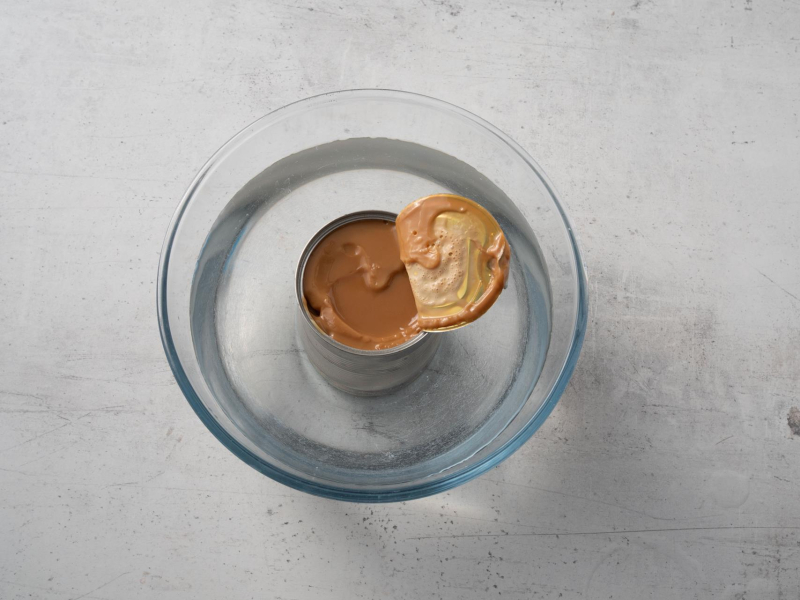 w szklanej misce z wodą puszka z ugotowanego mleka skondensowanego