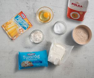 Na blacie kuchennym opakowanie twarogu, mąki, budyniu. Jajko w miseczce oraz erytrytol.