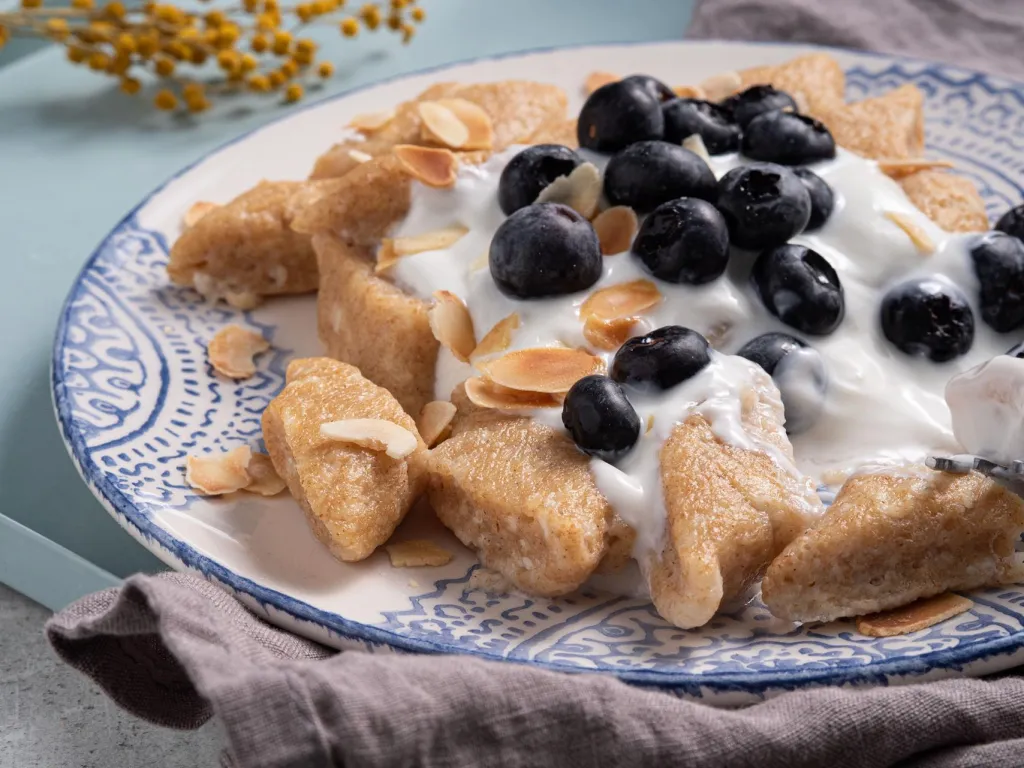 Fit pierogi leniwe z mąką orkiszową i twarogiem, podane z jogurtem i borówkami.