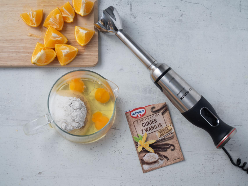 na blacie na desce pokrojona pomarańcza, obok w szklanym naczyniu pozostałe słądniki do blendowania na babkę z pomarańczą