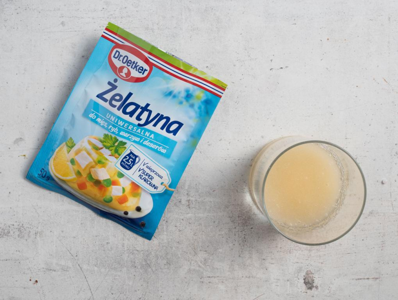 Żelatyna w opakowaniu na blacie kuchennym. W szklance namoczona żelatyna w szklance.