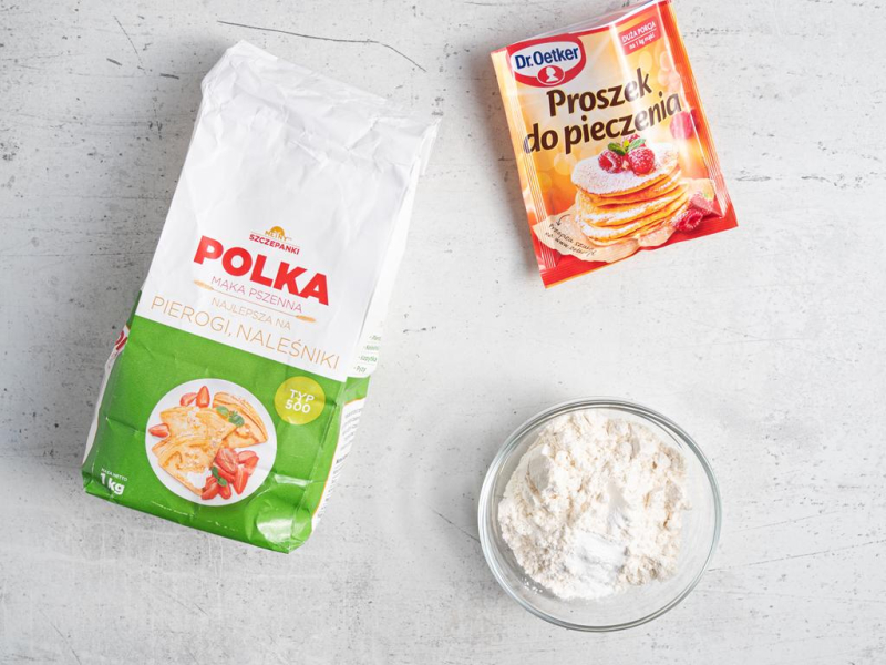 Opakowanie mąki na blacie kuchennym. Obok mąka w miseczce razem z proszkiem do pieczenia.