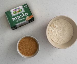 Na blacie kuchennym kostka masła. Obok cukier trzcinowy i mąka pszenna.