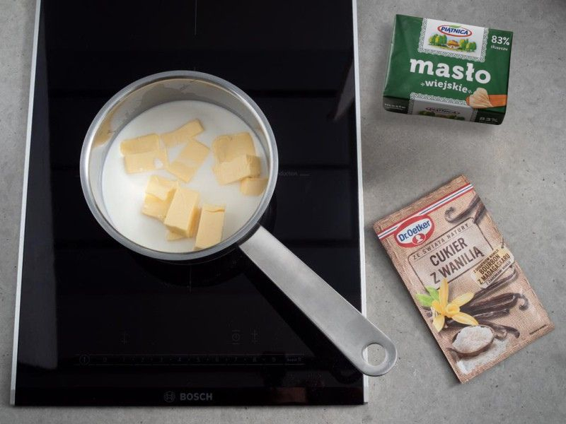 Na blacie masło, cukier z wanilią oraz garnek z wodą, mlekiem i masłem
