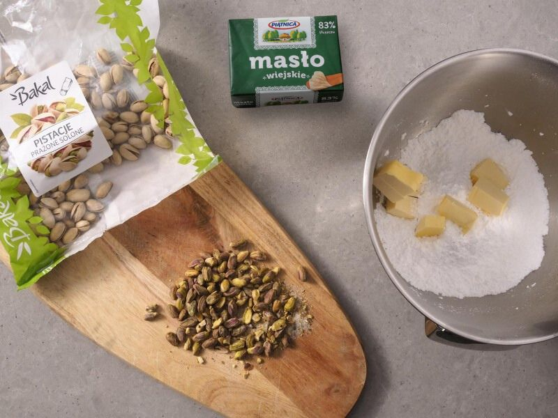 pokrojone bakalie na desce, obok miska z masłem kerrygold i cukier puder