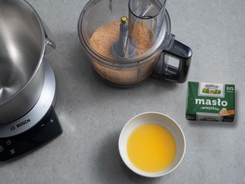 pokruszone ciasteczka na ciasteczkowy spód, obok masło