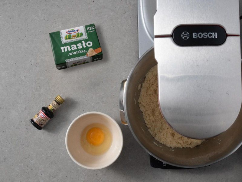 Na blacie robot kuchenny firmy Bosch. Obok w miseczkach składniki do ciasta kruchego i kostka masła