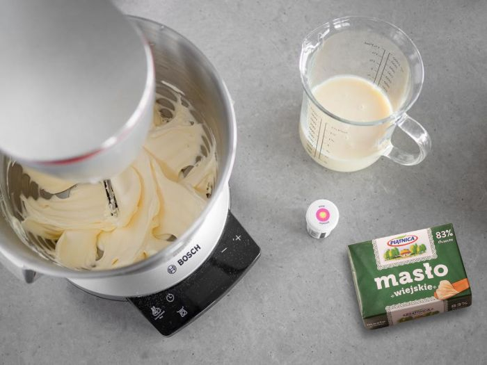 w misie robota ucierane masło obok w naczyniu mleko skondensowane i różowy barwnik Wilton